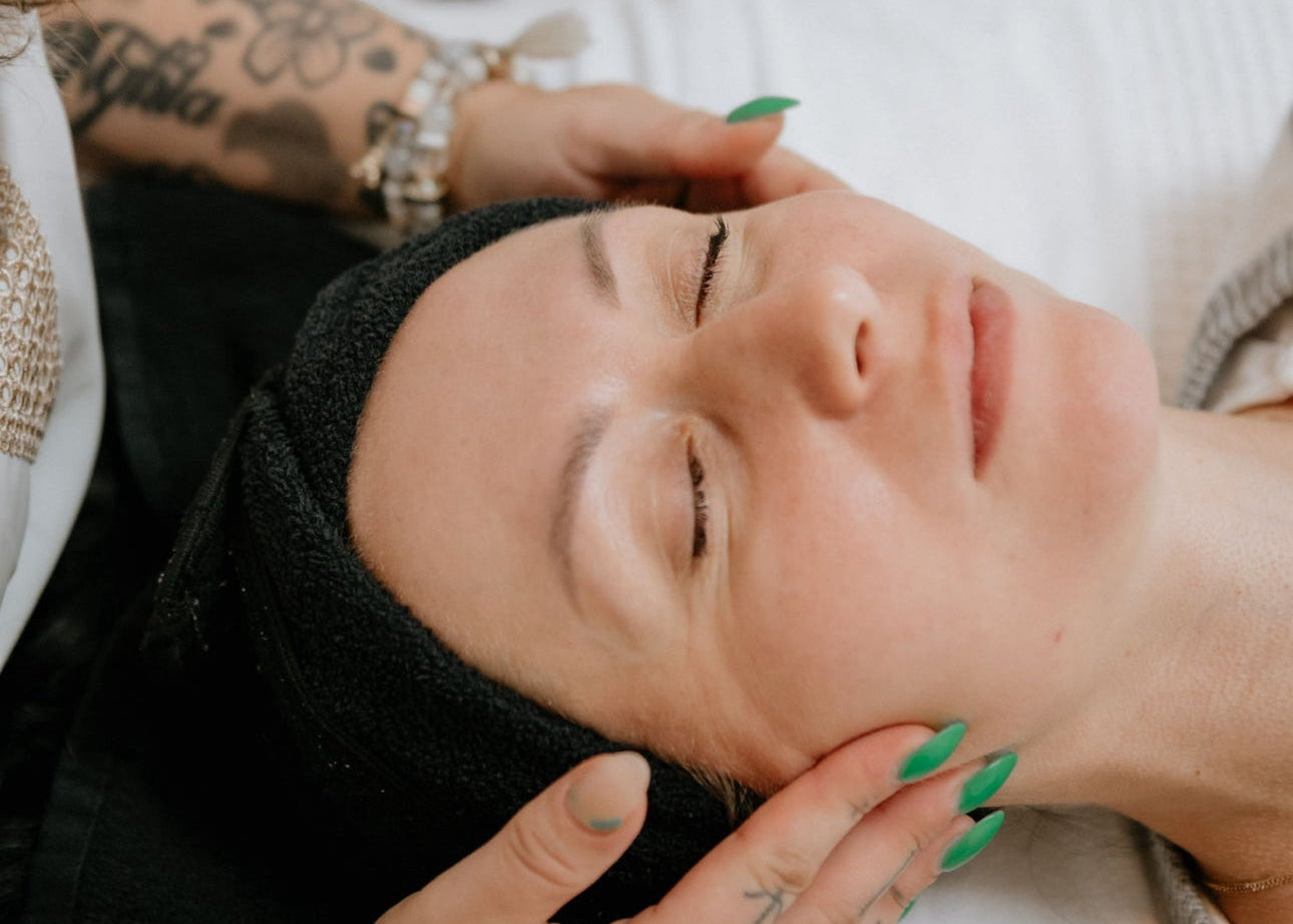 Person receiving a facial treatment with another person applying product to their face.