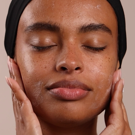 Close-up of a person with hands on their face against a neutral background